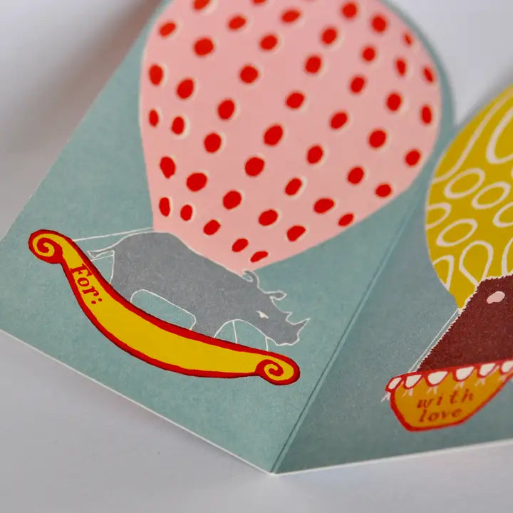 A close-up of a greeting card with a colorful hot air balloon holding a rhino. 