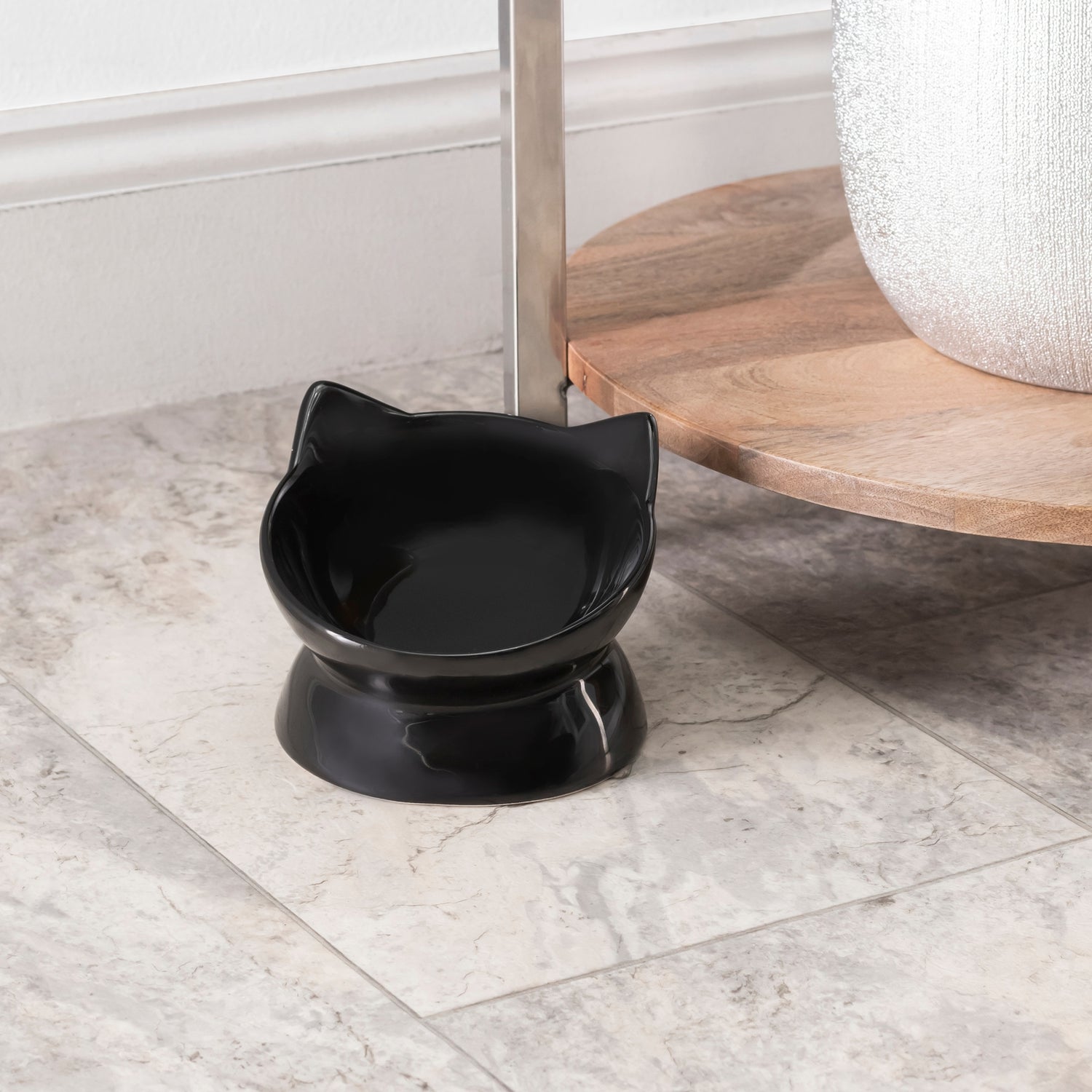 Black cat-shaped bowl on a marble floor with a wooden shelf in the background.