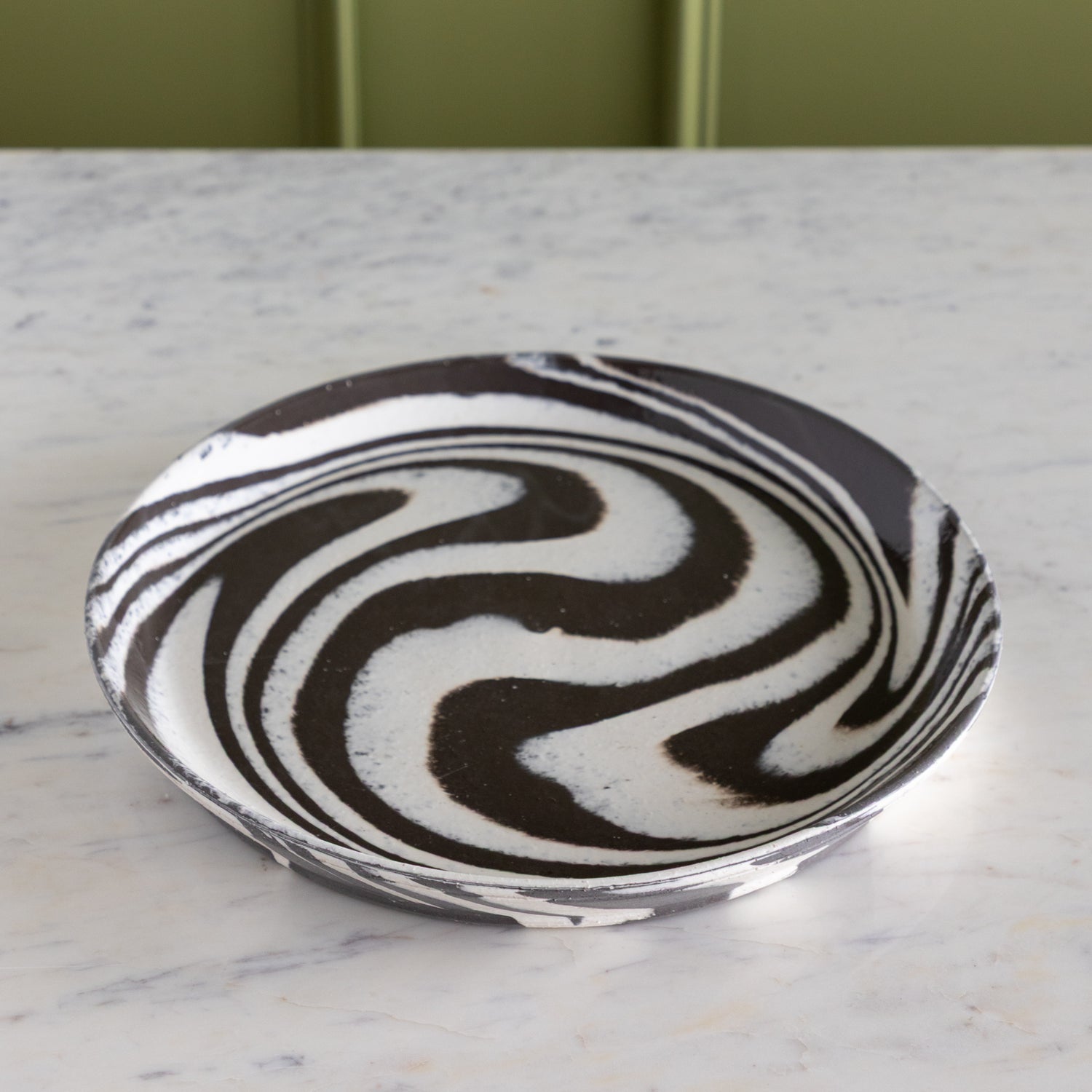 Decorative plate with black and white swirling pattern on a marble surface.
