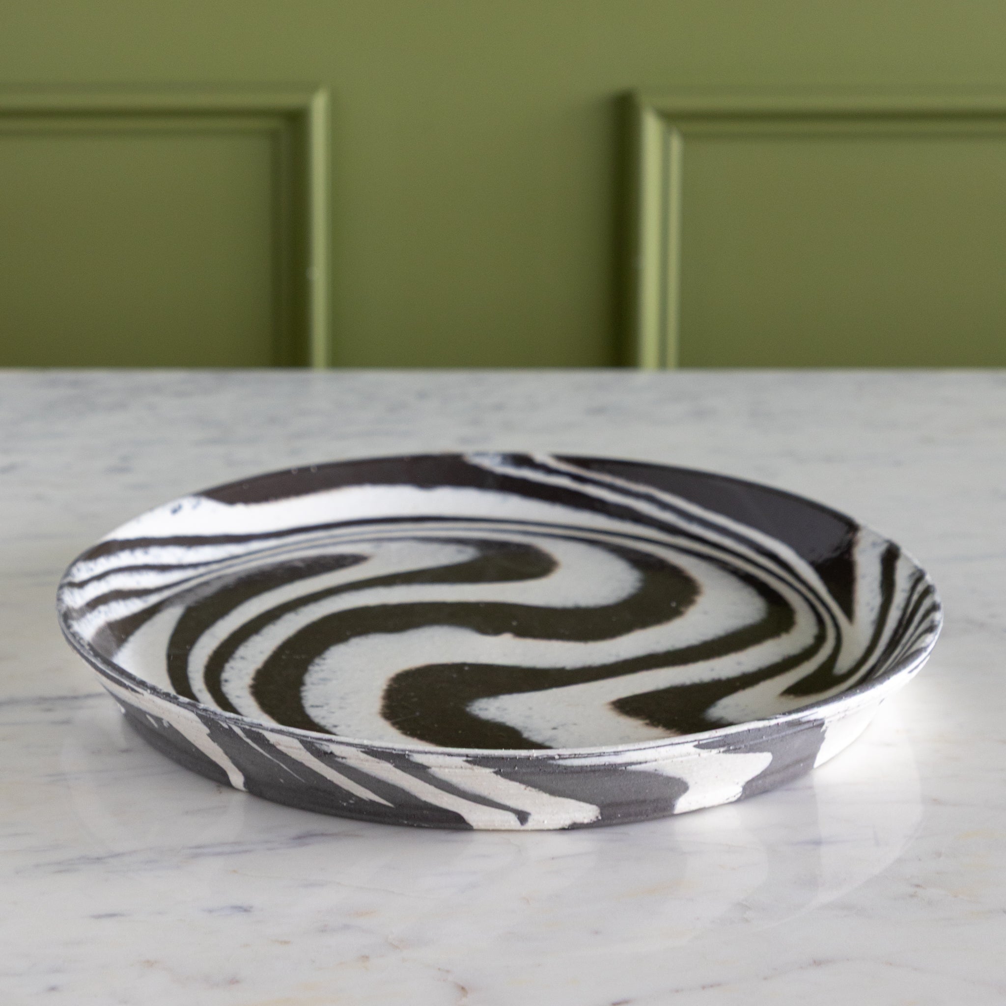 Black and white patterned ceramic plate on a marble surface with a green wall background.