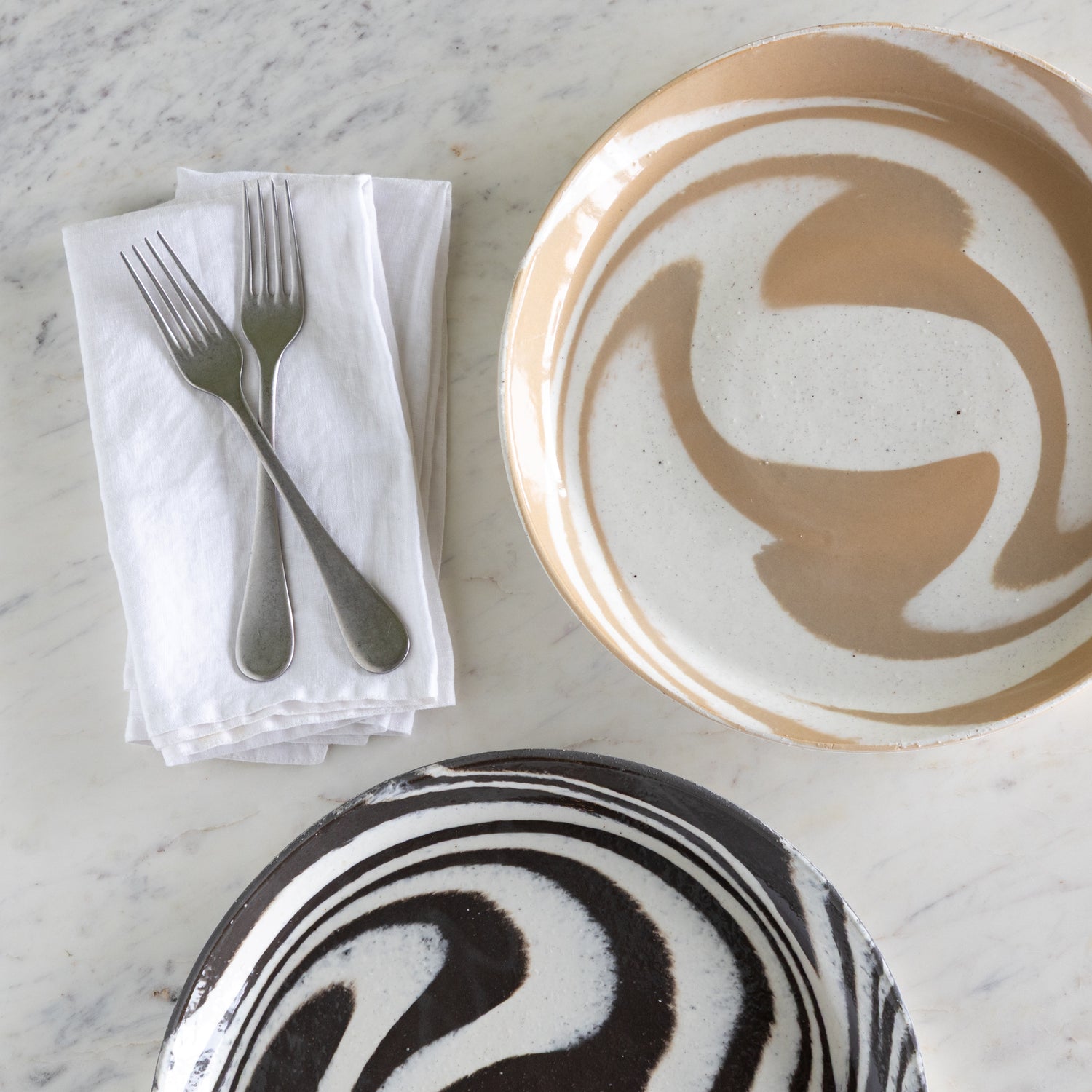 Two ceramic plates on a marble surface with cutlery and napkin.