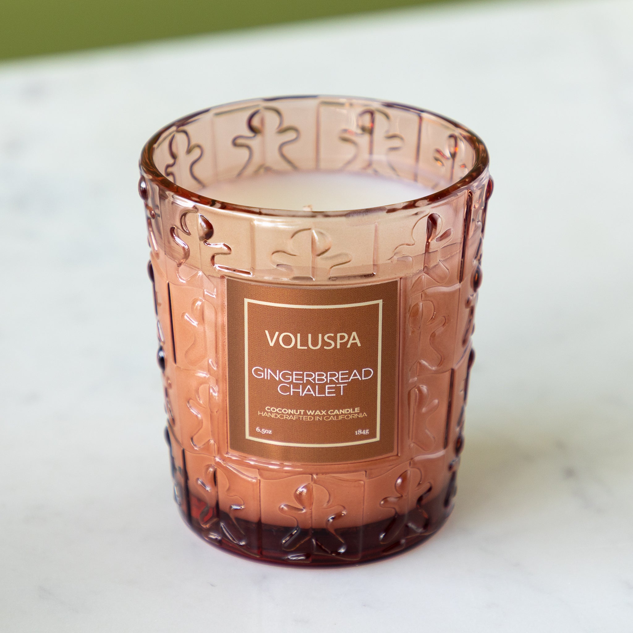 Decorative candle in a patterned glass holder with Voluspa branding on a white background.