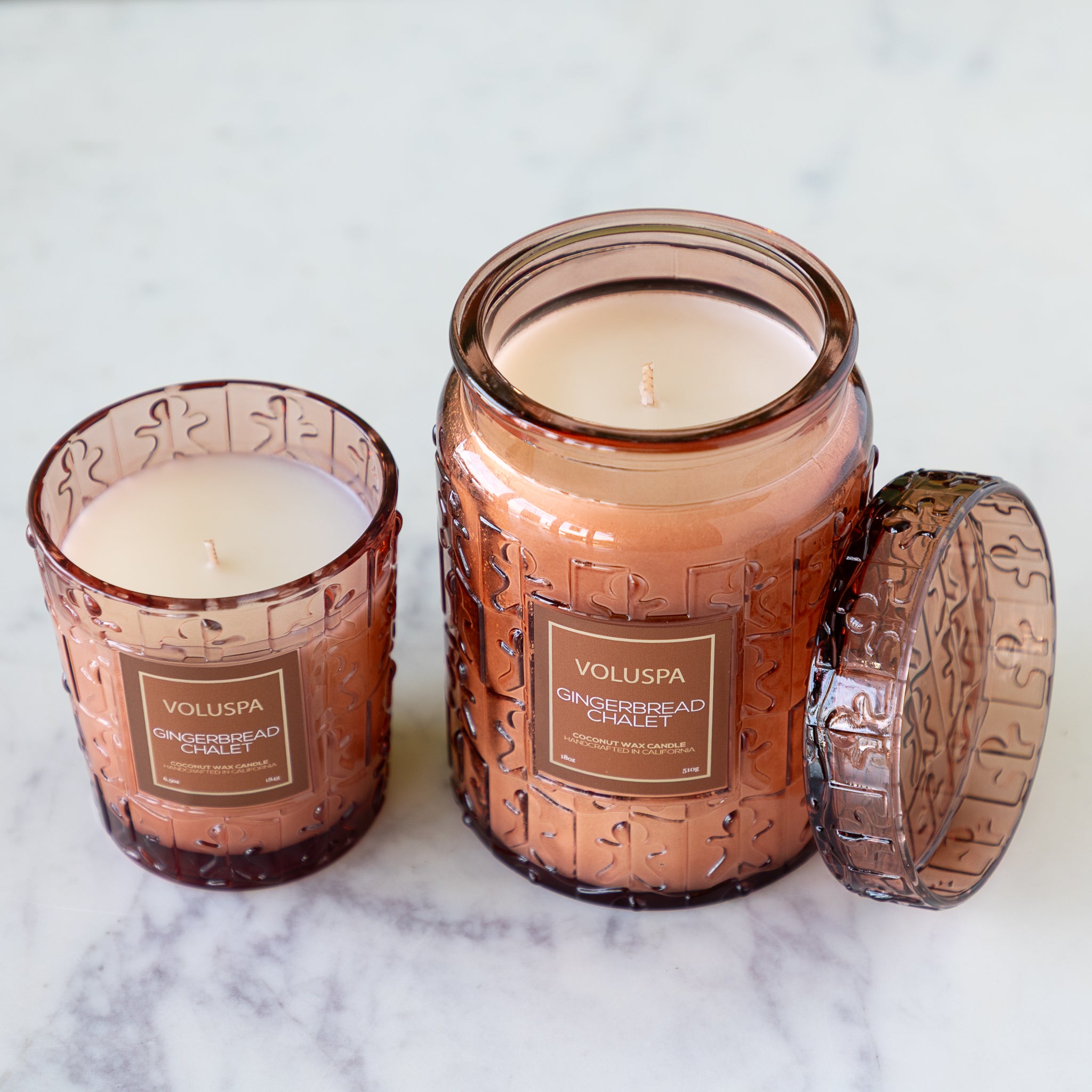 Two Voluspa candles in decorative jars on a marble surface.