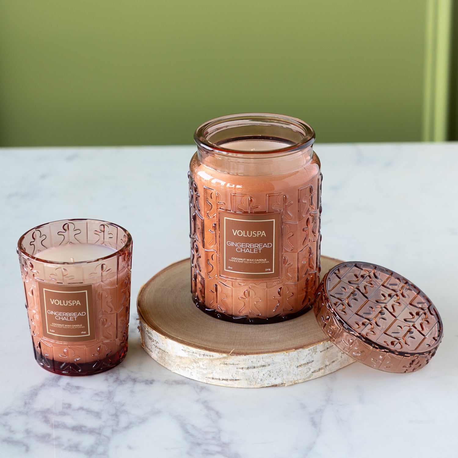 Two Voluspa gingerbread man candles on a marble surface with a green background.
