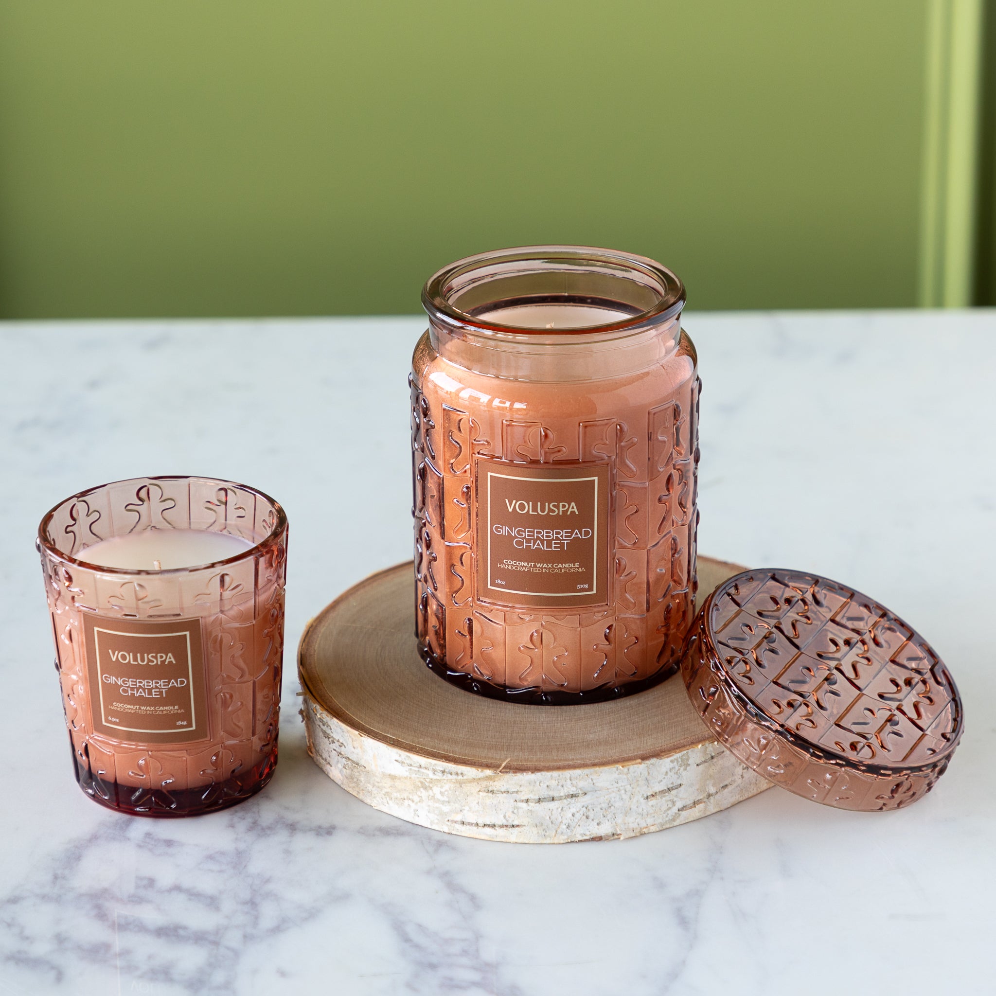 Two Voluspa gingerbread man candles on a marble surface with a green background.