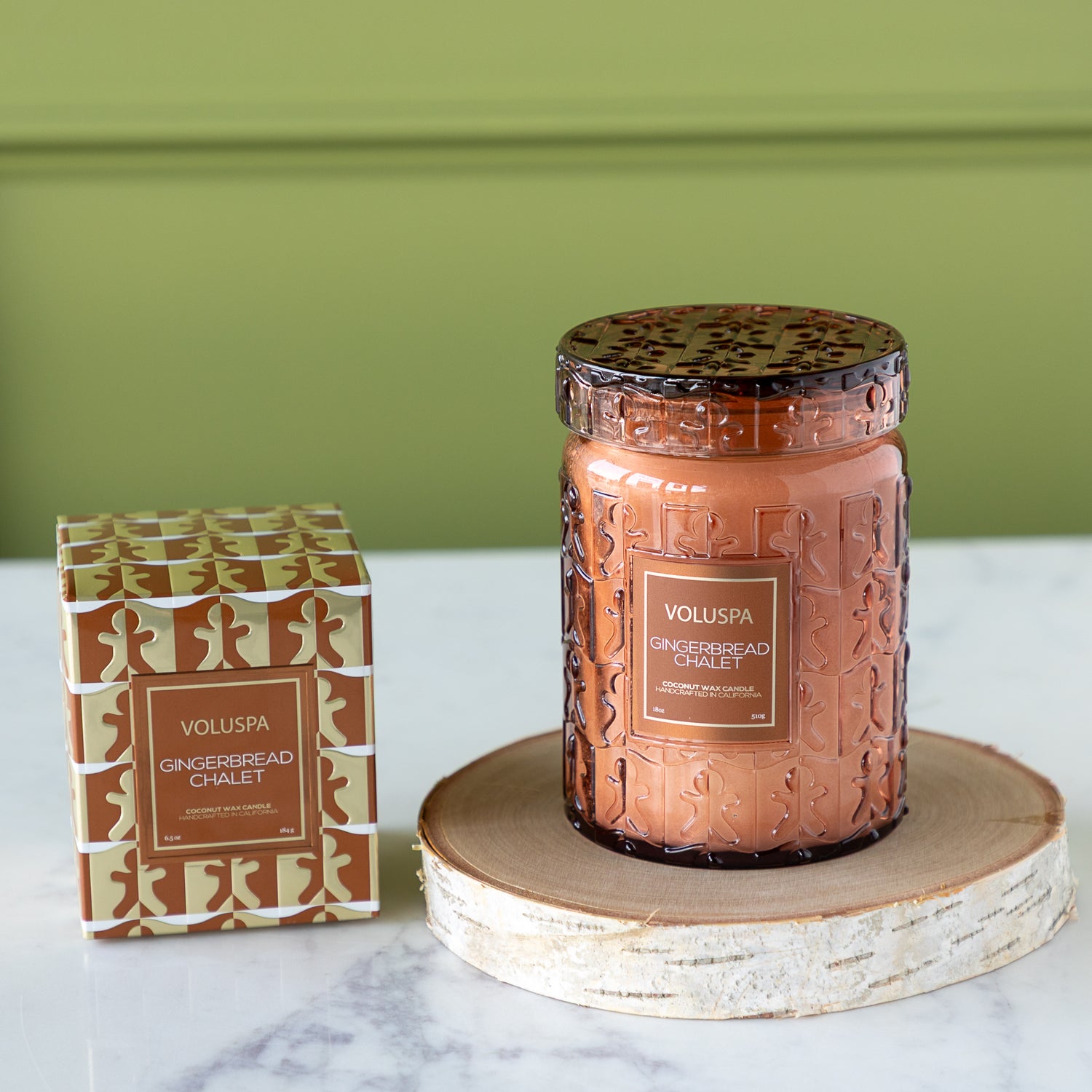 Voluspa candle and packaging on a marble surface with a green wall background.
