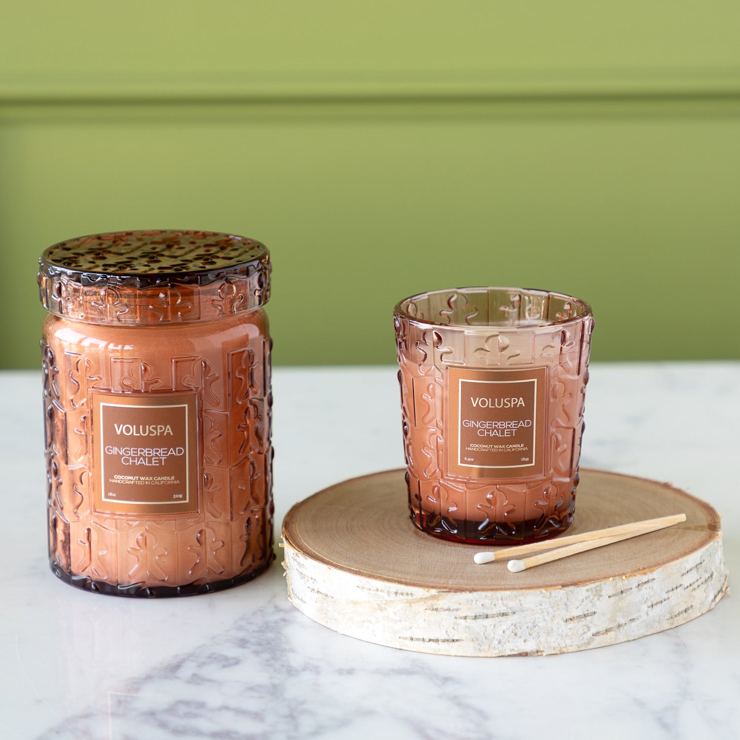 Two Voluspa candles on a marble surface with a green background.
