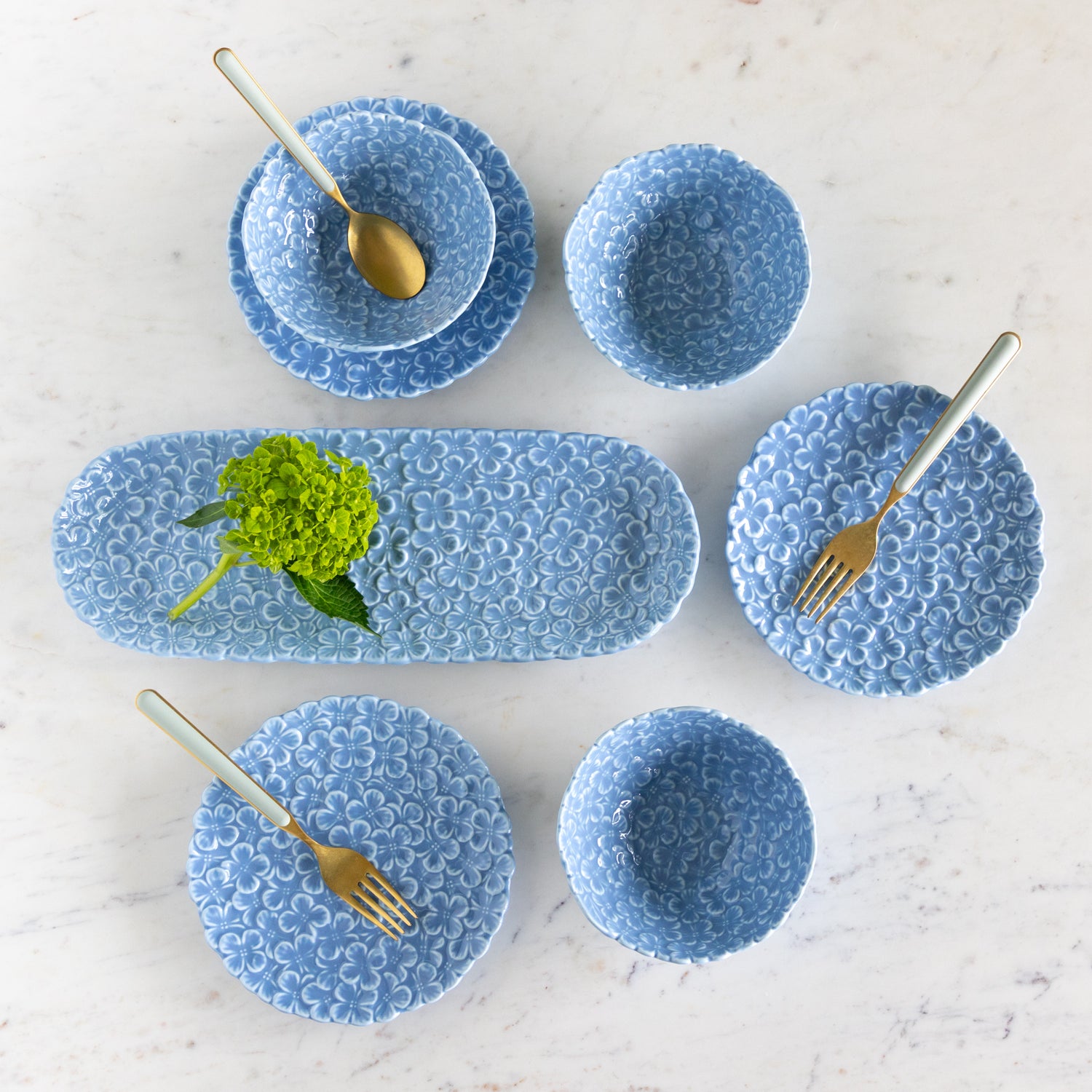 Set of blue textured ceramic dishes with gold cutlery on a light background.
