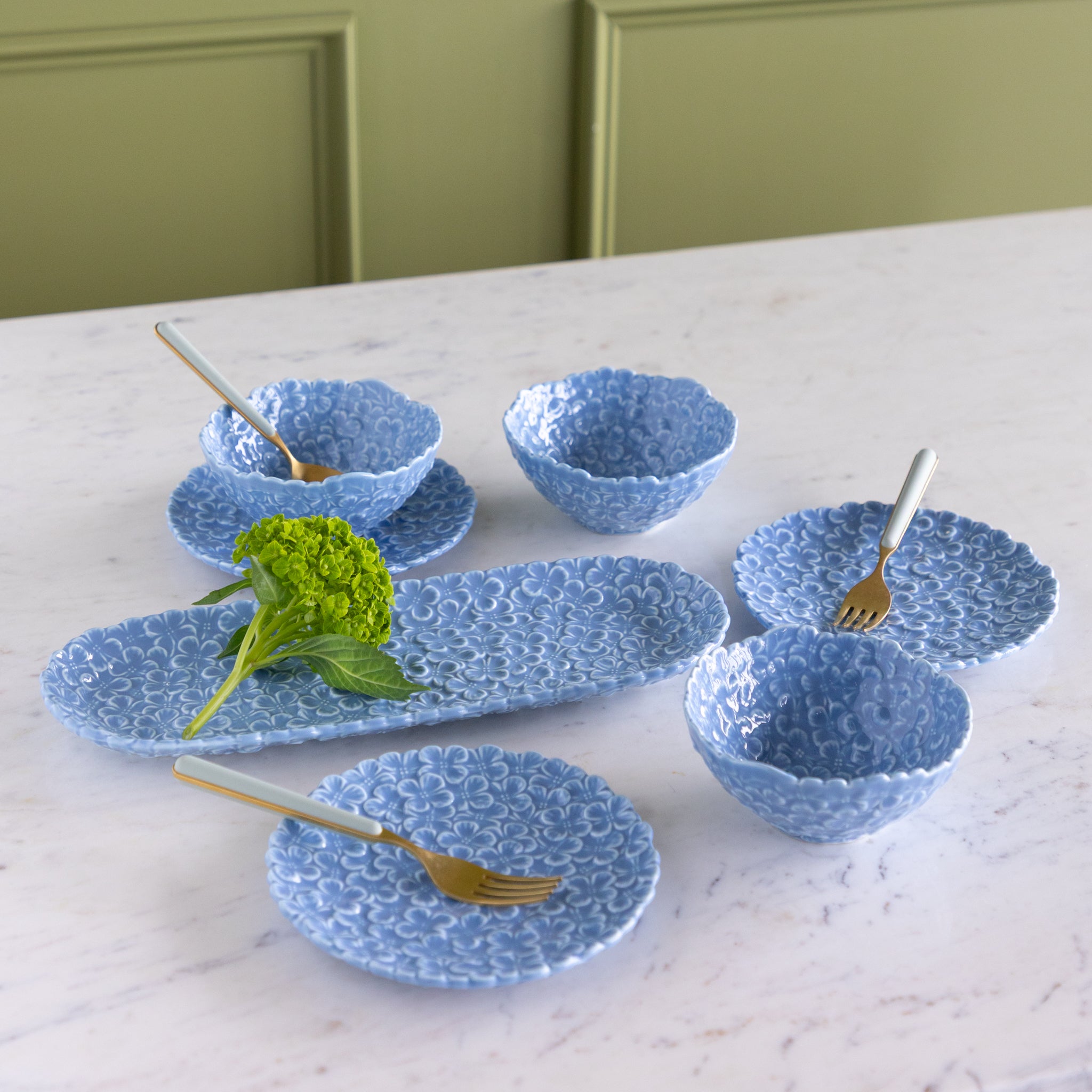Set of blue textured bowls and plates on a marble surface with greenery.