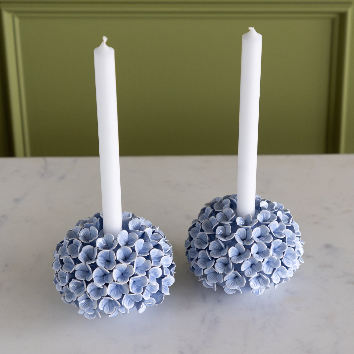 Two candle holders made of blue hydrangea flowers with white candles on a marble surface.