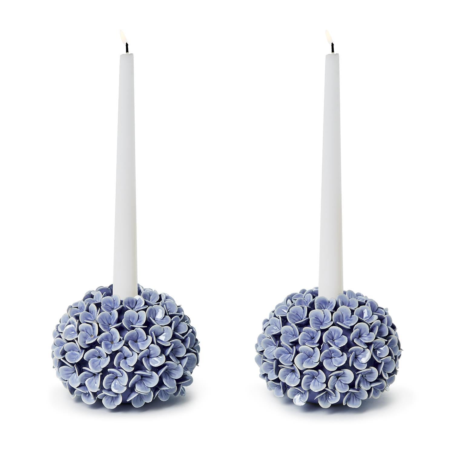 Two candle holders with hydrangea design holding white candles on a white background.