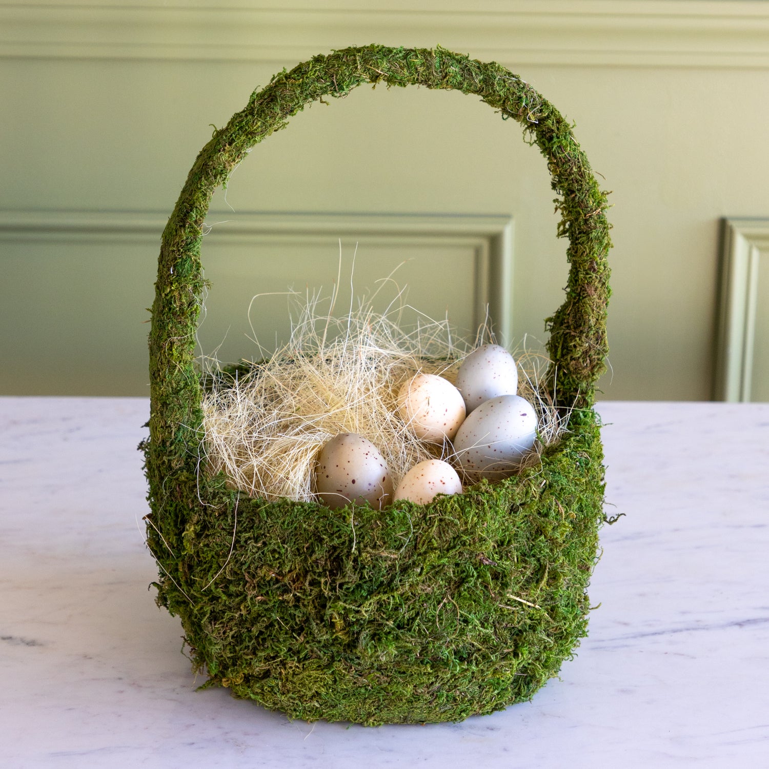 Moss-covered basket with decorative eggs on a neutral background.
