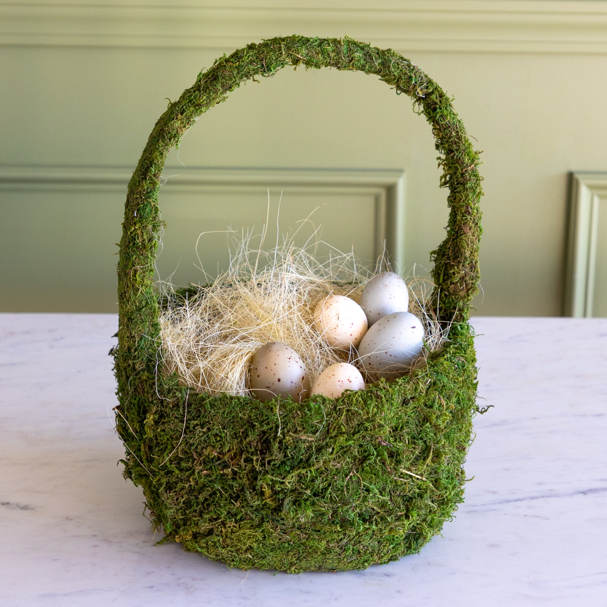 Moss-covered basket with decorative eggs on a neutral background.