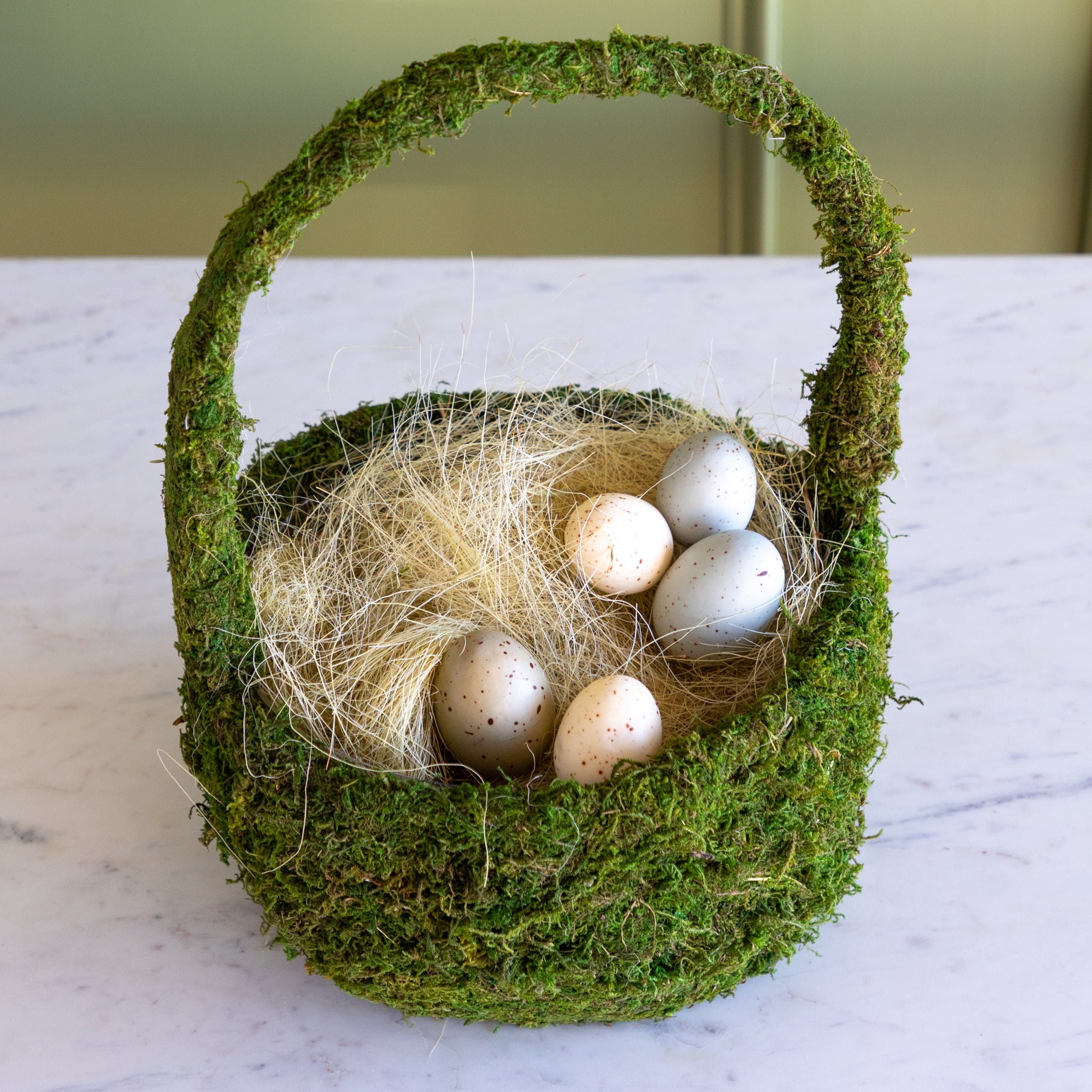 Moss-covered basket with filler and eggs on a marble surface.