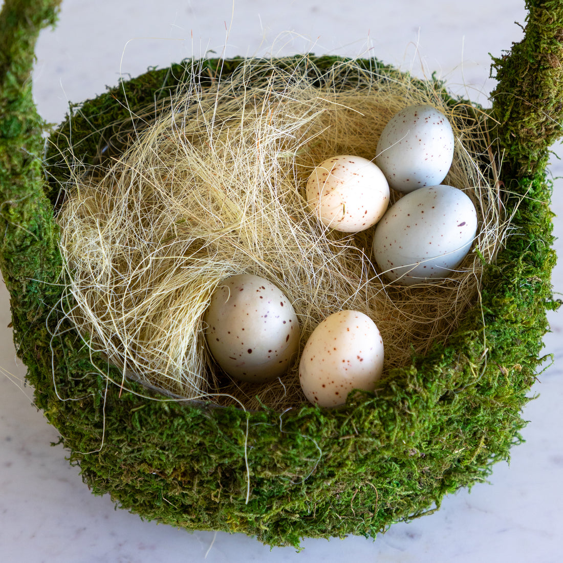 A moss basket with basket filler and eggs on a marble table.
