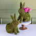 Two moss-covered bunny-shaped planters with one holding pink flowers on a white surface.