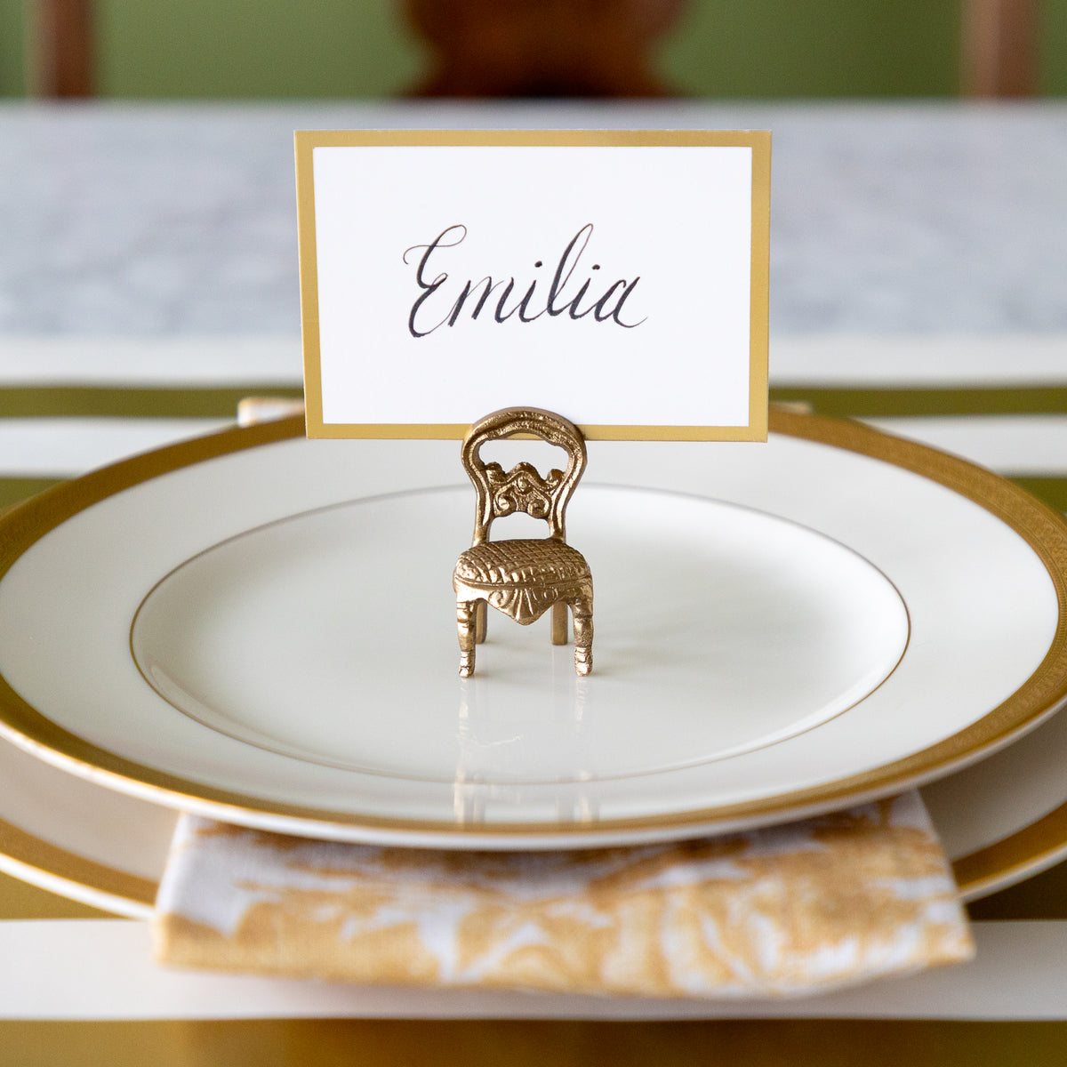 A gold miniature chair place card holder holding a white card with the name &