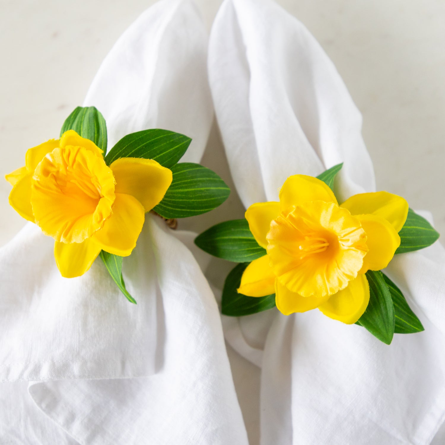 Daffodil Spray Napkin Ring Holders around two white linen napkins.