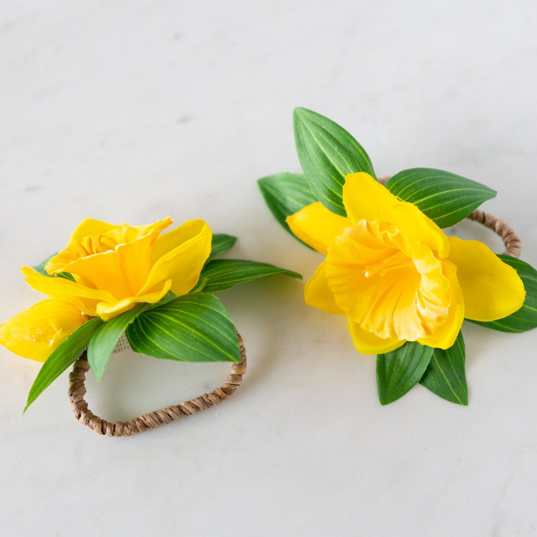 Two Daffodil Spray Napkin Ring Holders with rattan holders on a marble surface.