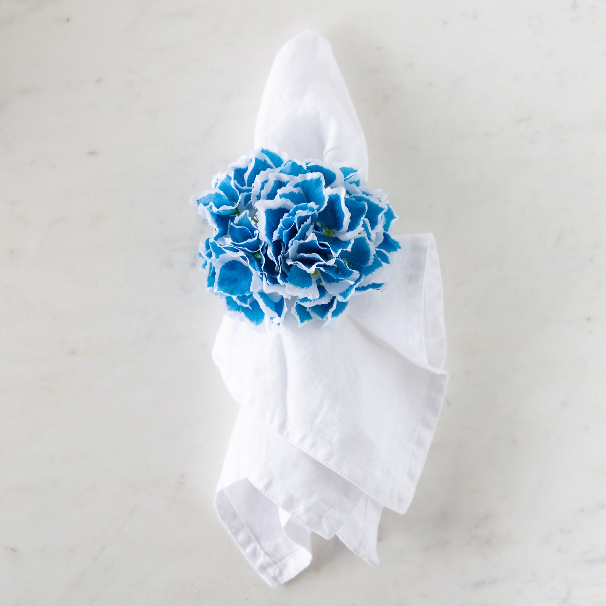 White napkin with a blue Border Hydrangea Napkin Ring on a marble surface.