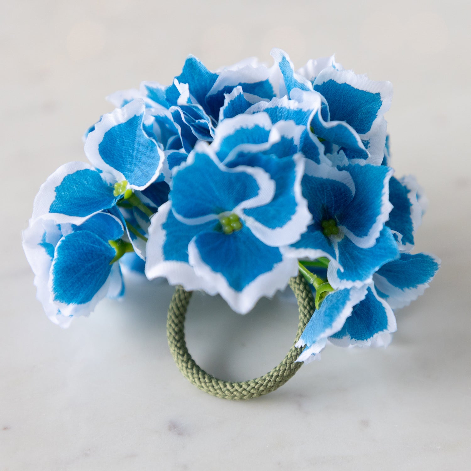 A blue Border Hydrangea Napkin Ring with a green rope holder on a marble surface.