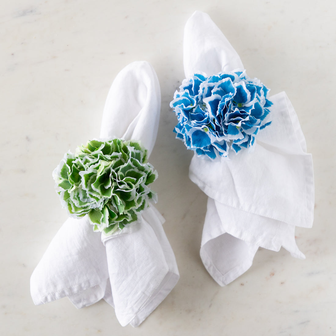 Two white napkins with Border Hydrangea Napkin Rings in green and blue.