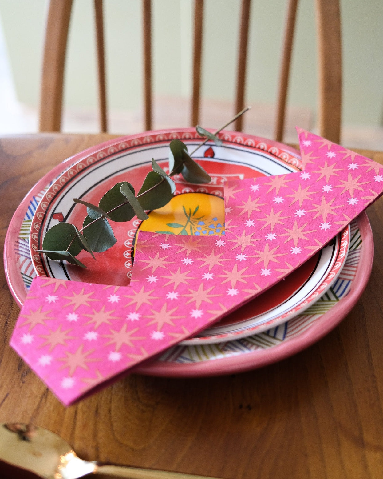 Stack of plates with a pink paper party hat on the plates on a wooden table.