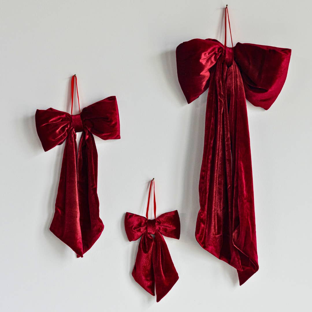 Three red oversized bows made of red velvet hanging on a white wall.