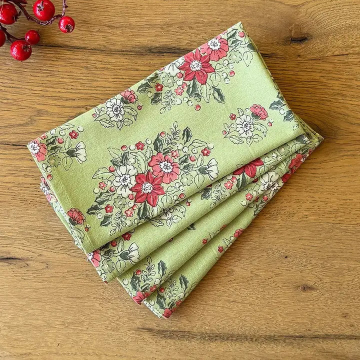 A folded piece of light green fabric with a red, white, and gray floral pattern, displayed on a wooden tabletop with red berries in the corner.