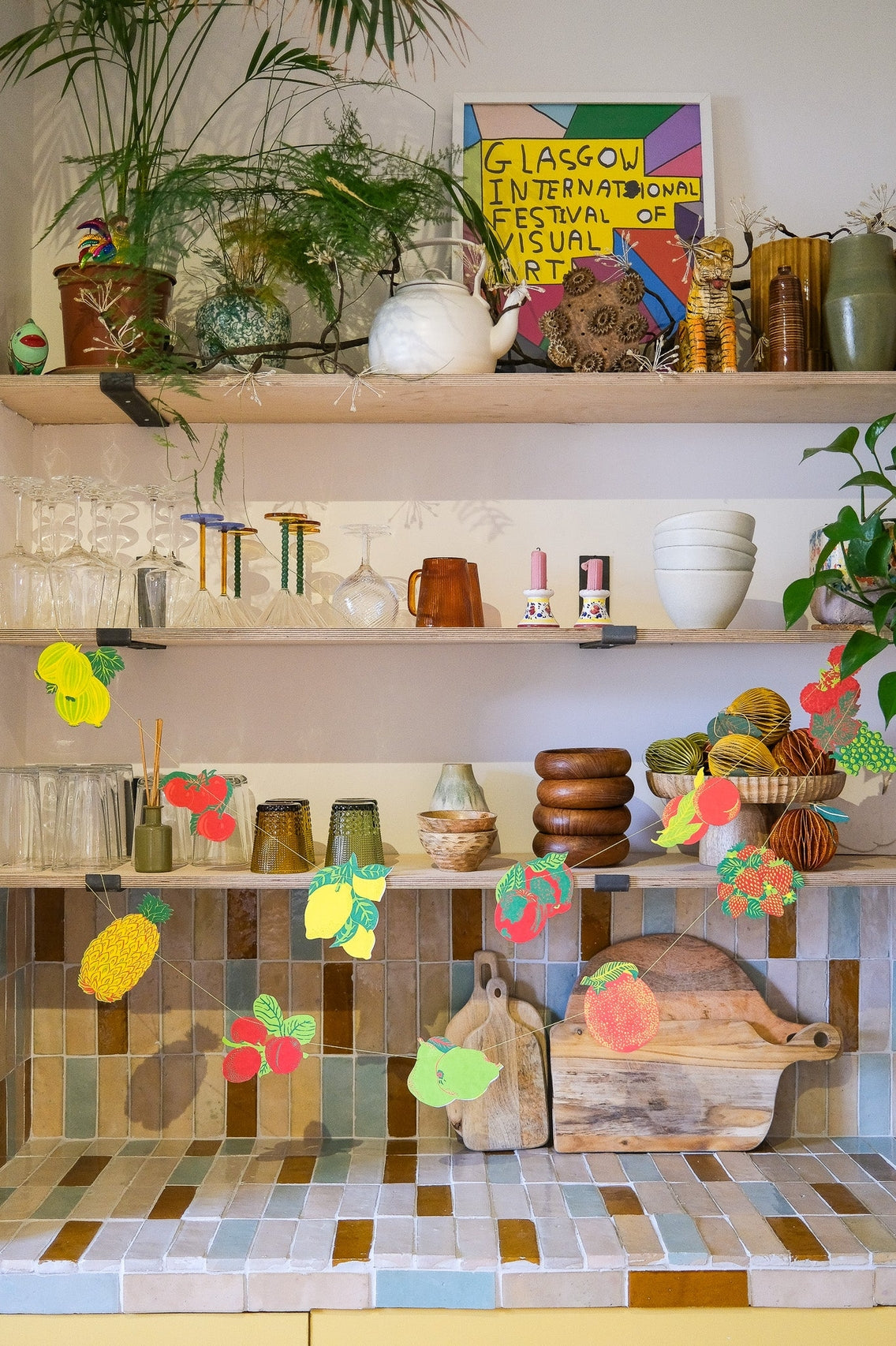 Shelves with decorative items, plants, and a colorful sign on a tiled wall.