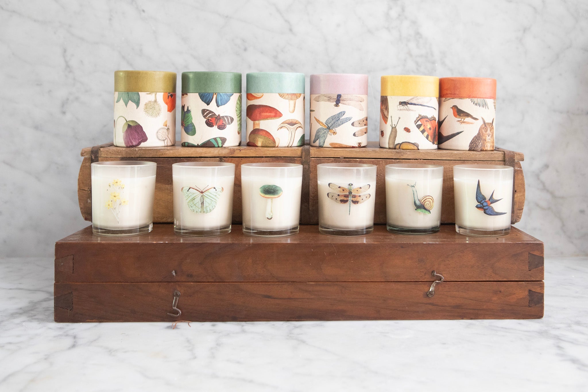 Set of candles with nature-themed designs on a wooden stand against a marble background.