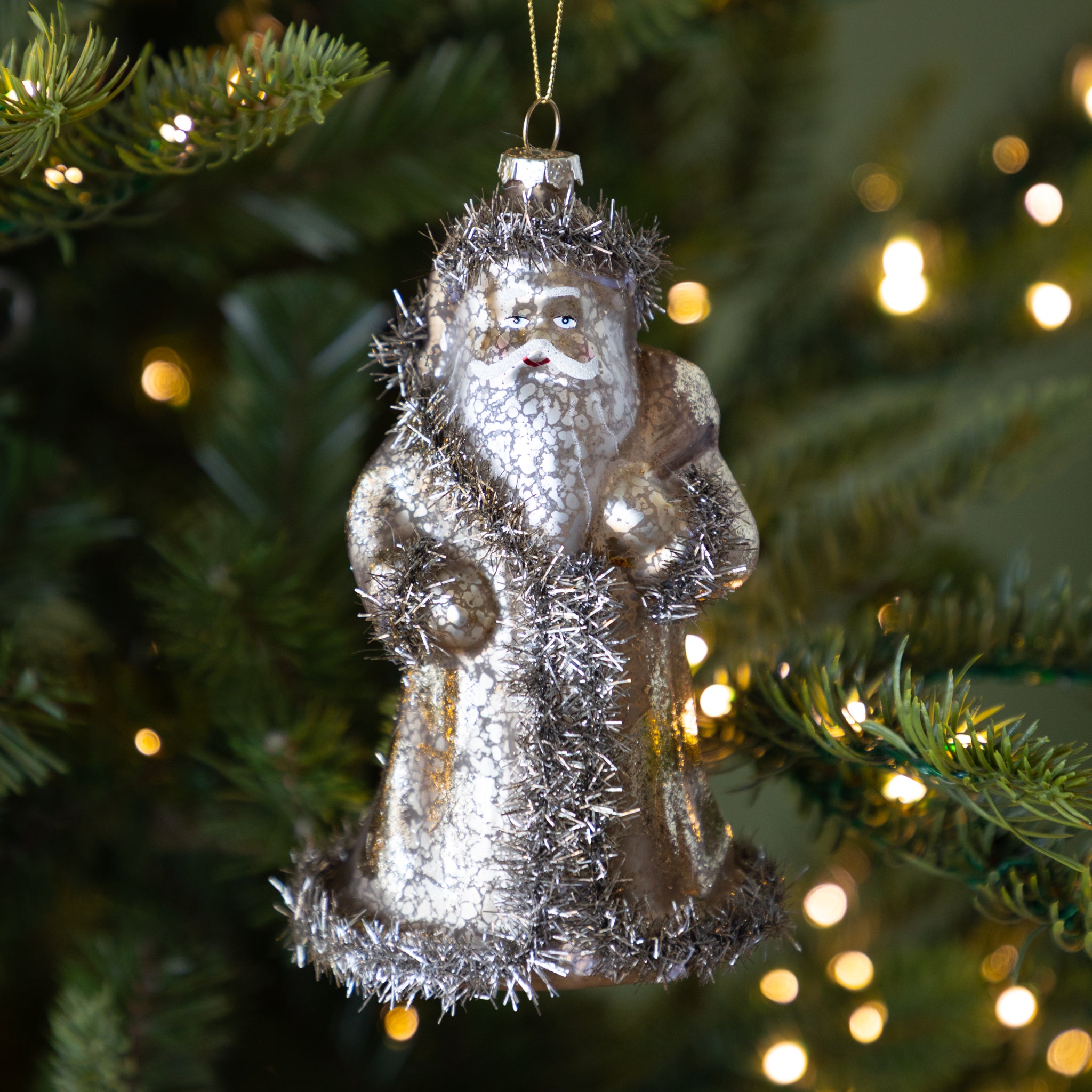 Decorative Christmas ornament resembling Santa on a tree with lights in the background.