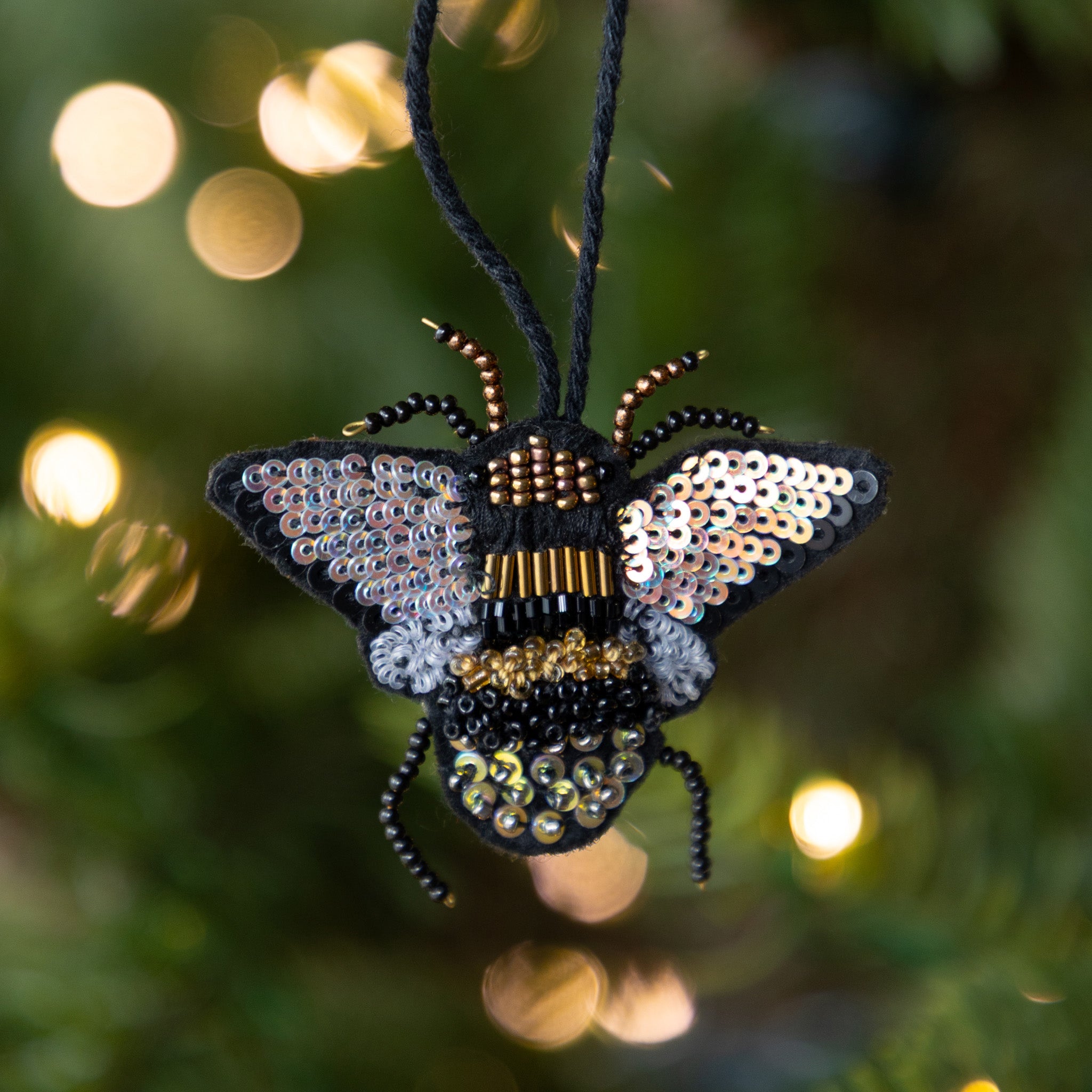 Decorative bee ornament with sequins against a blurred festive background.