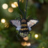 Decorative bee ornament with sequins against a blurred festive background.