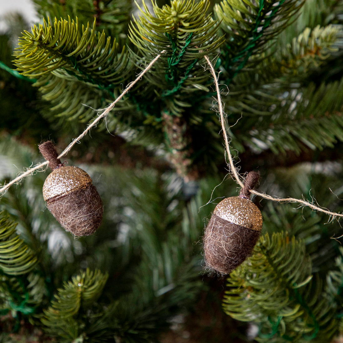 Close up of woolen acorn garland in a tree showing its glittered top .