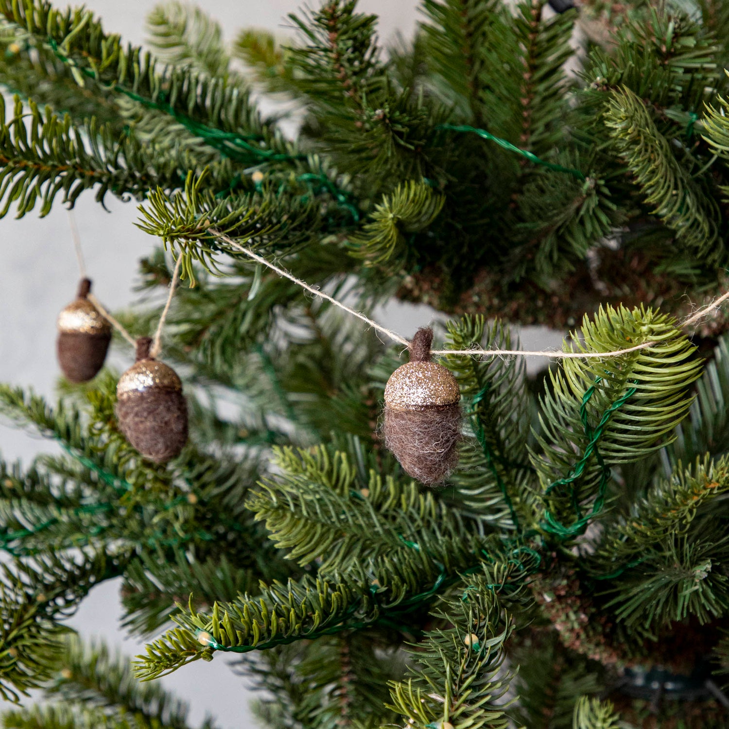 Close up of woolen acorn garland in a tree showing its glittered top .