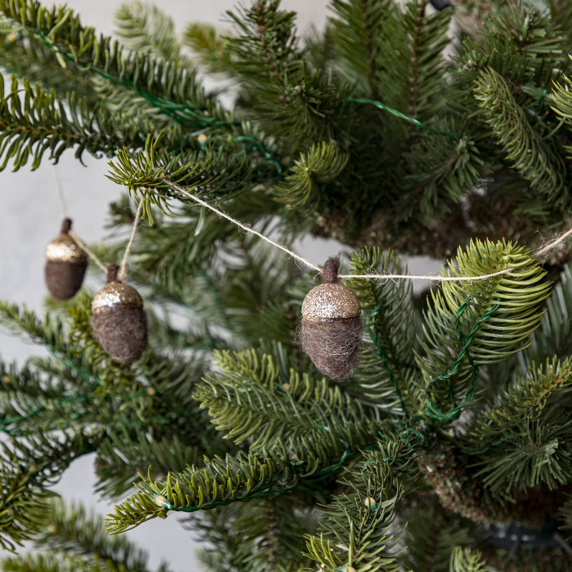 Close up of woolen acorn garland in a tree showing its glittered top .