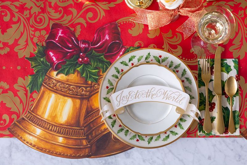 Christmas-themed place setting with gold bell, red bow, and &