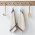 Two beige towels with blue stripes hanging on a wooden rack with kitchen utensils.