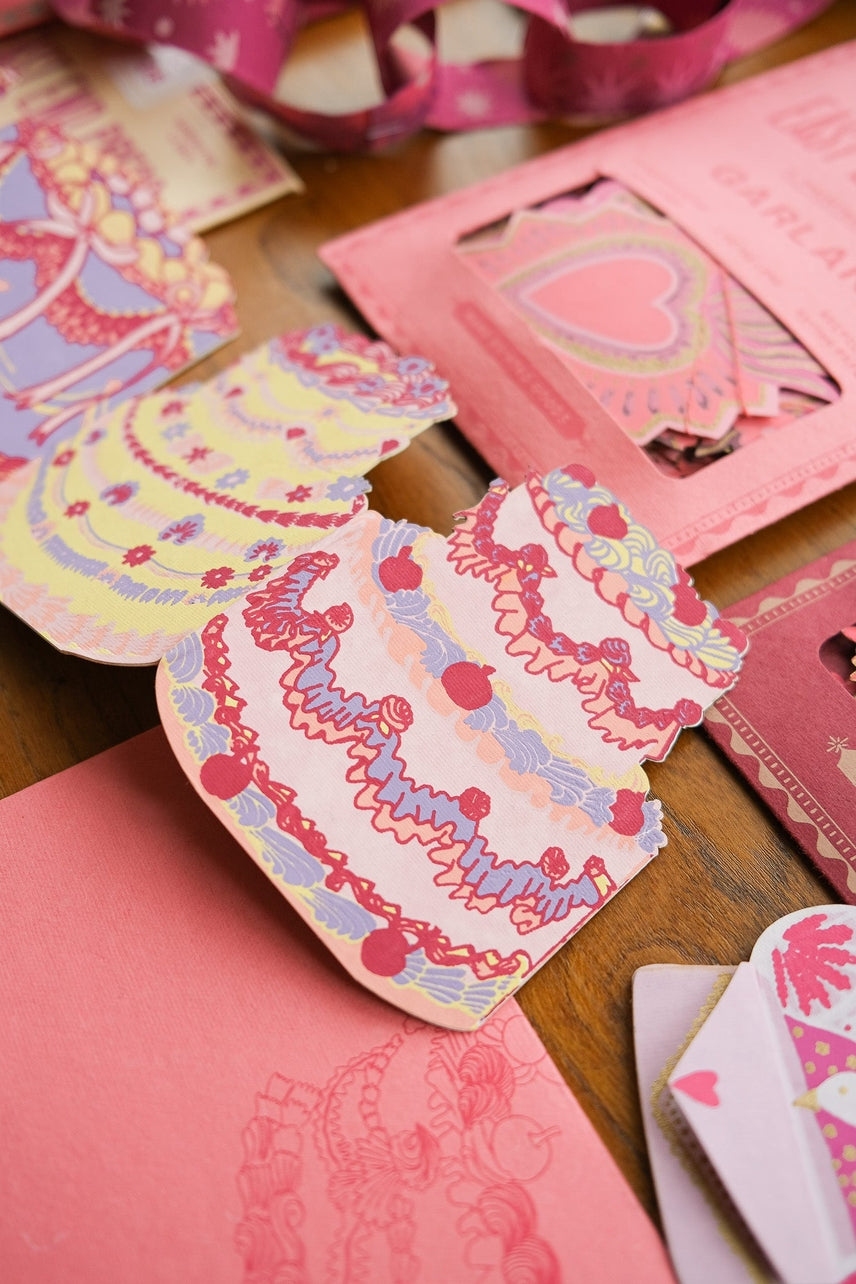 Colorful cardstock with decorative patterns on a wooden surface in the shape of decorated birthday cakes.