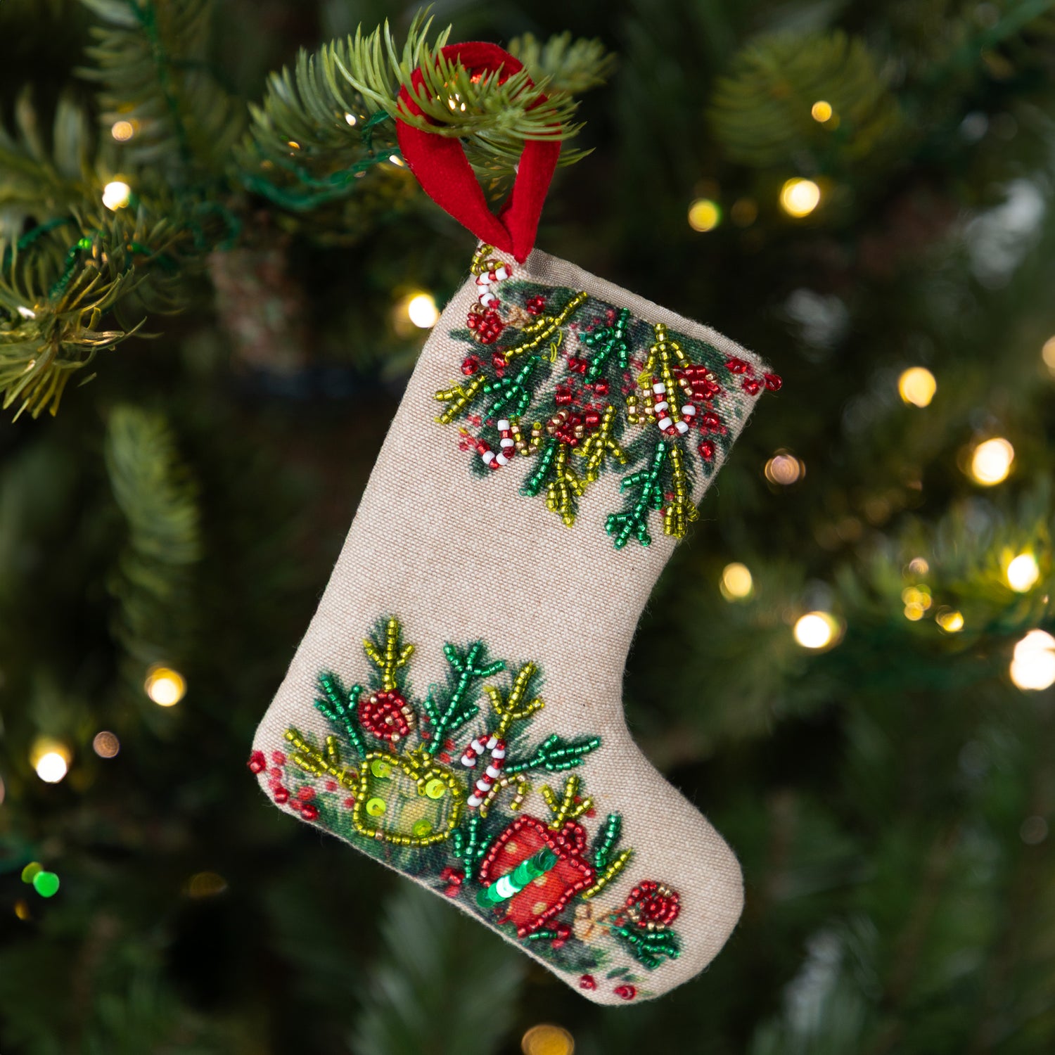 Decorative Christmas stocking with festive patterns and a beaded design hanging on a tree by a red loop.