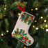 Decorative Christmas stocking with festive patterns and a beaded design hanging on a tree by a red loop.