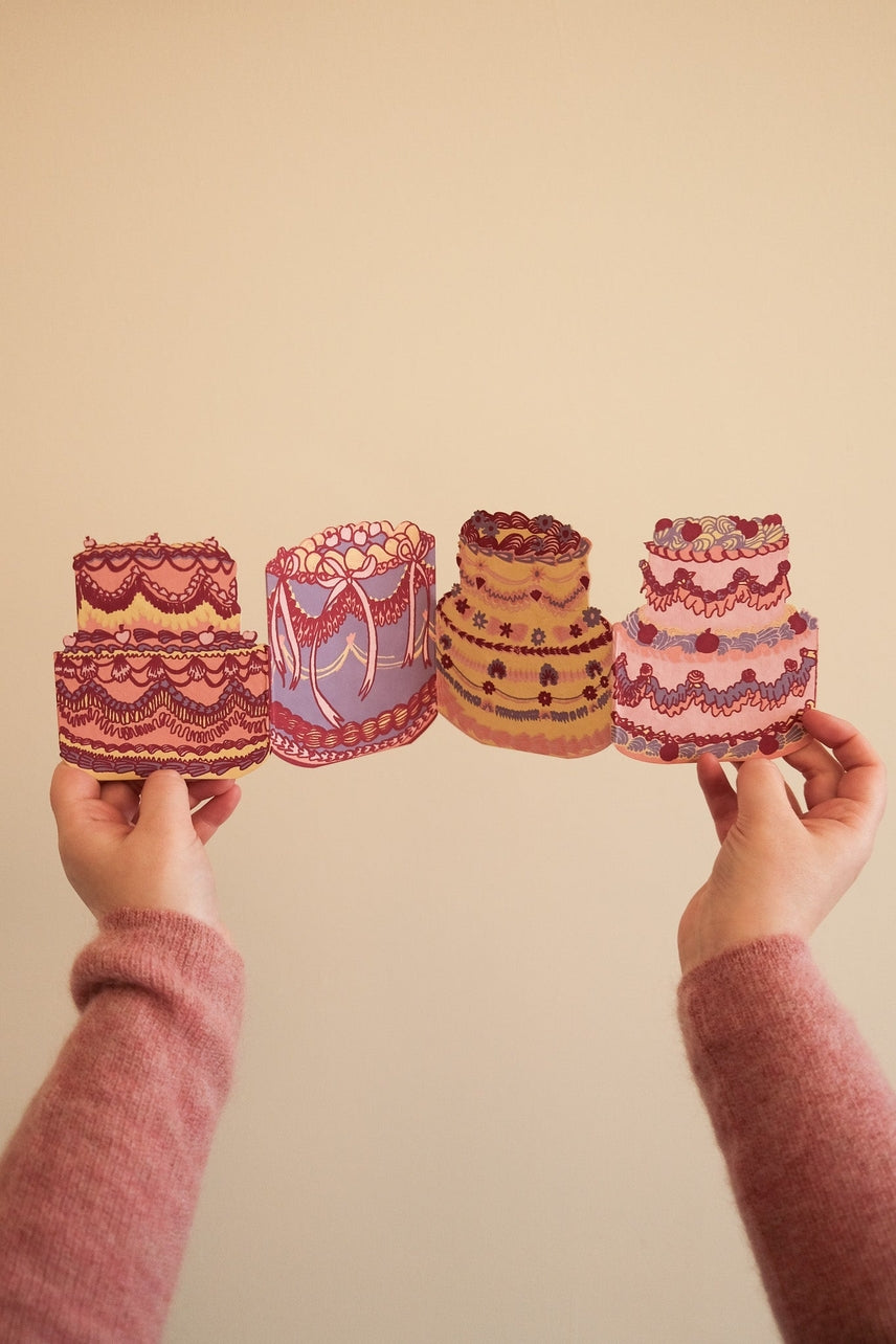 Two hands holding concertina cake card against a beige background.
