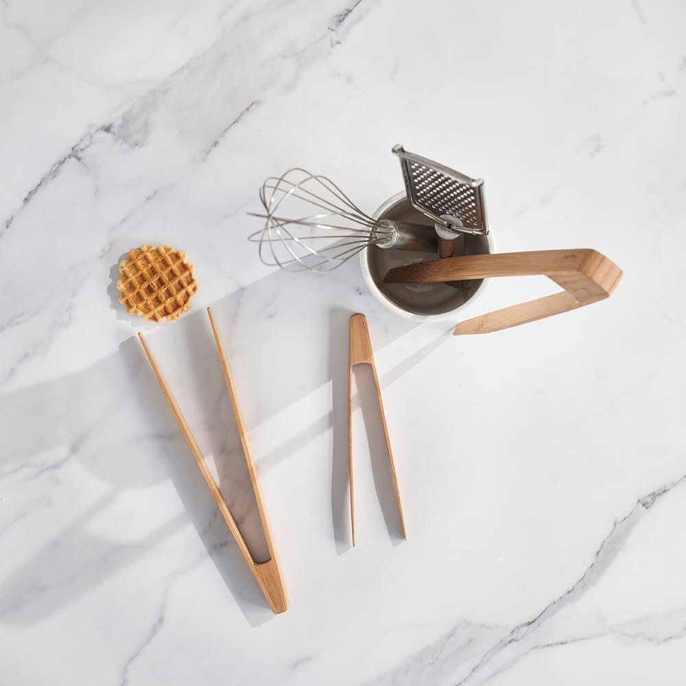 Wooden kitchen tools including a whisk, spatula, and spatula holder on a marble surface.