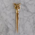 A polished gold-toned metal letter opener with an intricately detailed fox head handle, resting vertically on a white and gray veined marble surface.