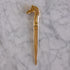 A polished gold-toned metal letter opener with a sculpted horse head handle, displayed vertically on a white and gray veined marble surface.