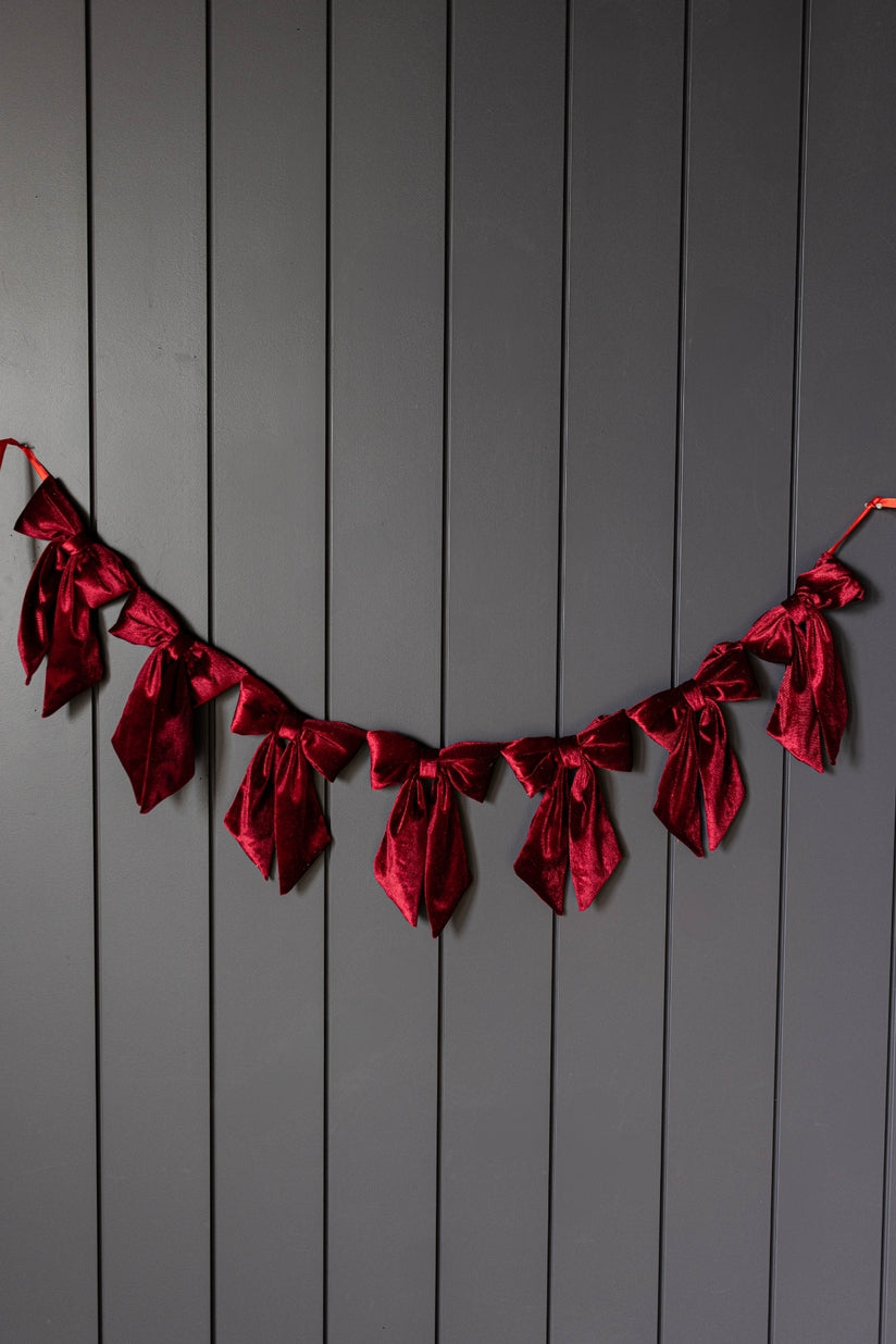 A red velvet bow garland hanging against a dark gray vertical wood-paneled wall.