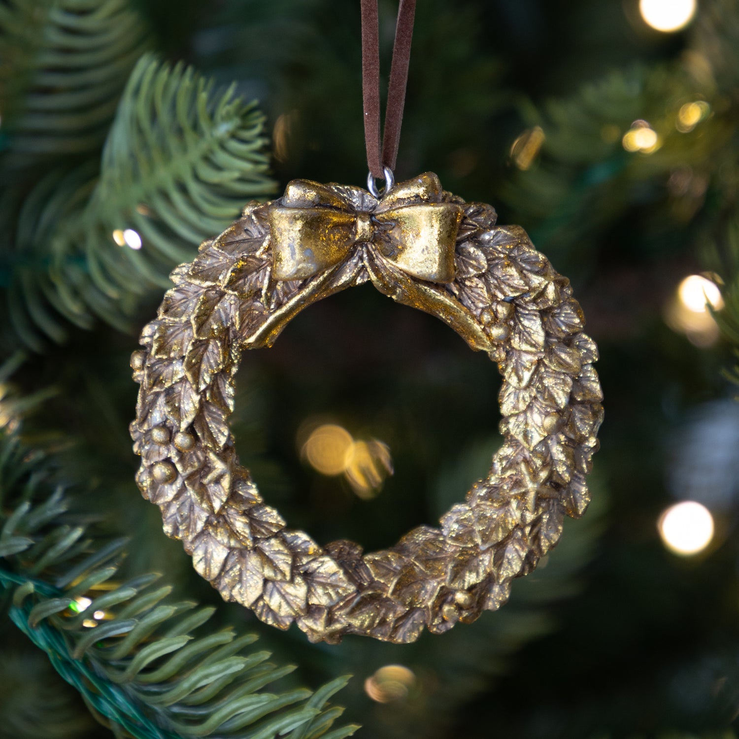Gold wreath ornament with a bow on a Christmas tree.