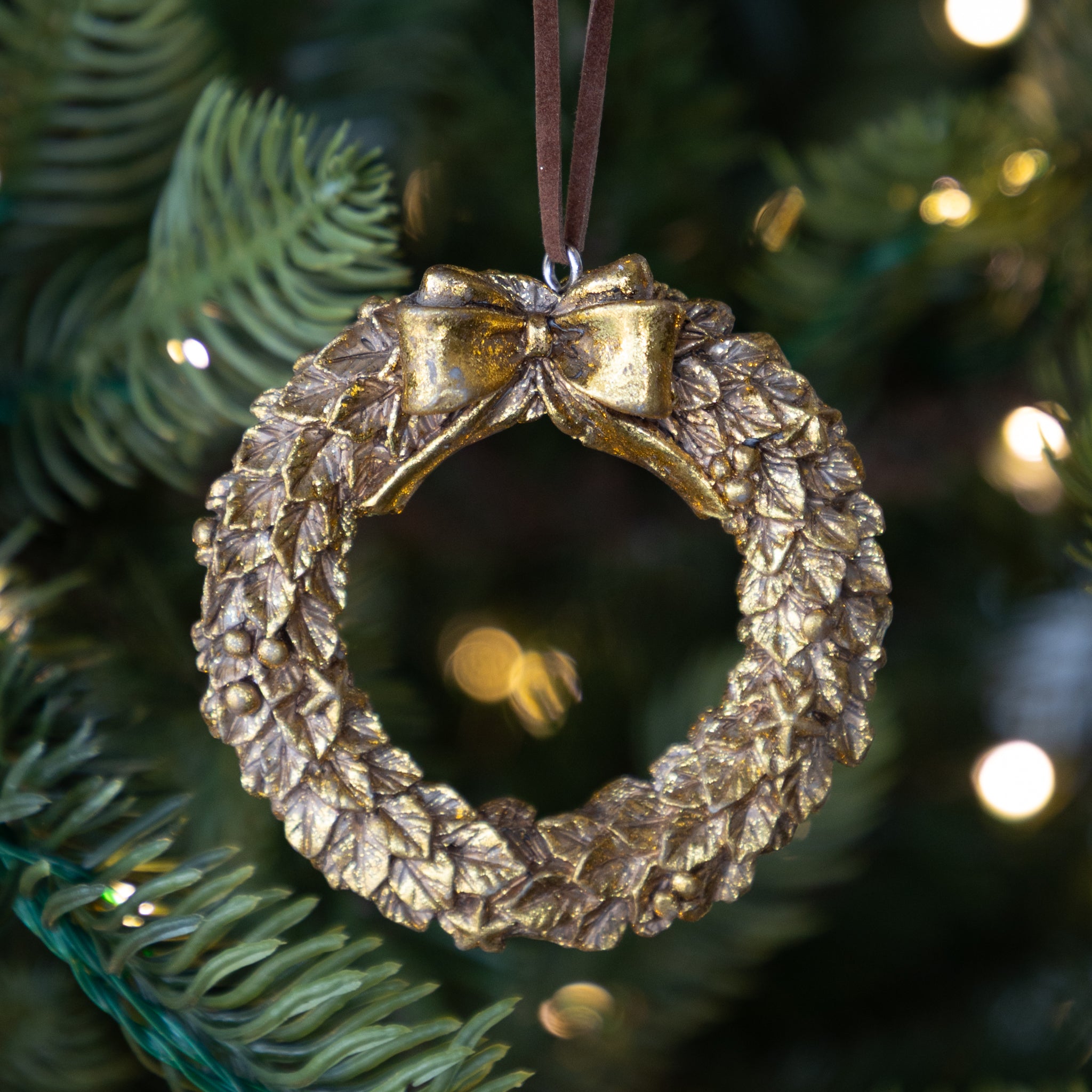 Gold wreath ornament with a bow on a Christmas tree.