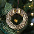Gold wreath ornament with a bow on a Christmas tree.